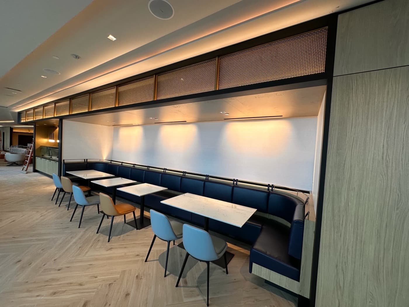 Dining alcove featuring a built-in banquette, illuminated timber canopy, and pale stone tables