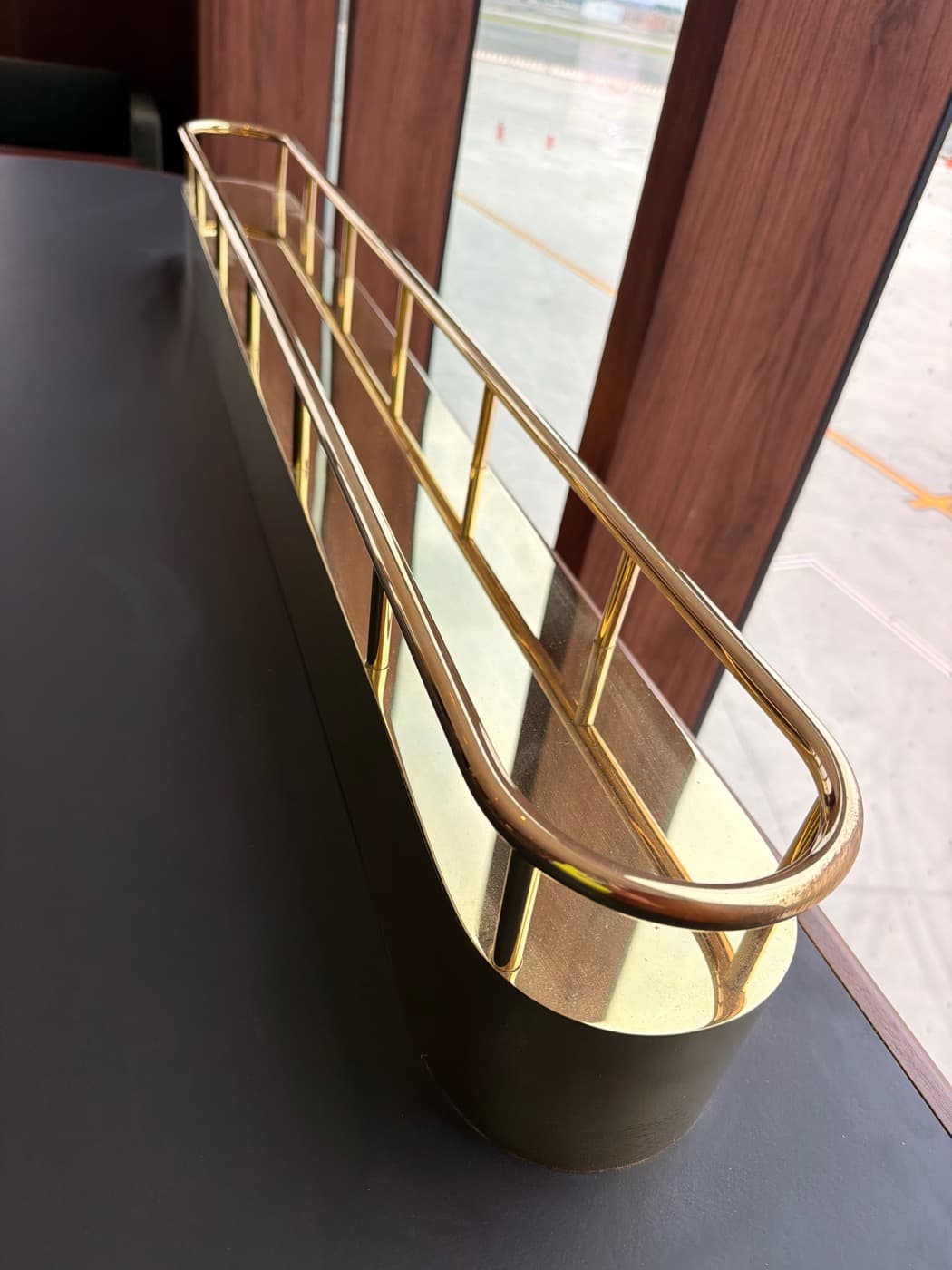 Polished brass rail detail mounted on a dark countertop beside timber wall panelling