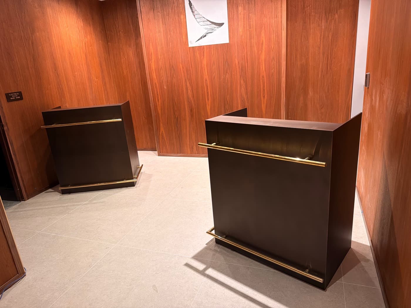 Reception area with warm timber wall panelling and two dark podiums featuring brass rails