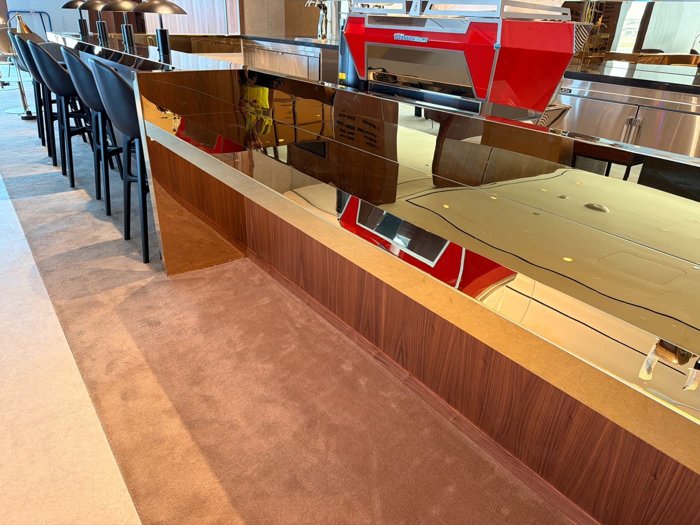 Commercial bar featuring wood-toned timber panelling, a polished metallic countertop, and bar stools