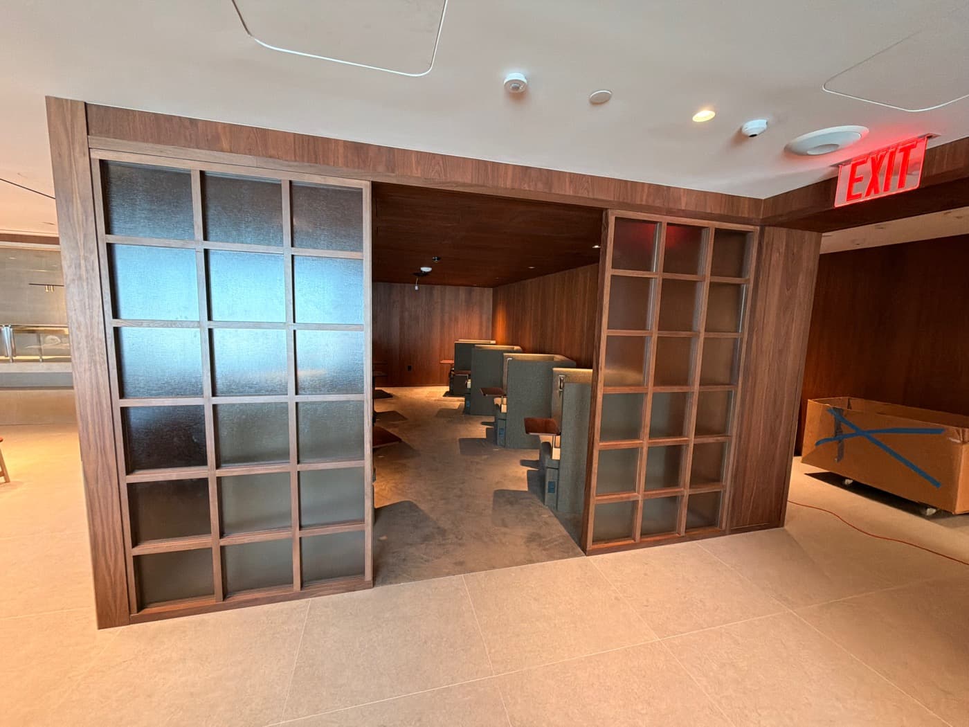 Lounge entrance framed by timber gridded glass partitions opening into wood-panelled private booth seating