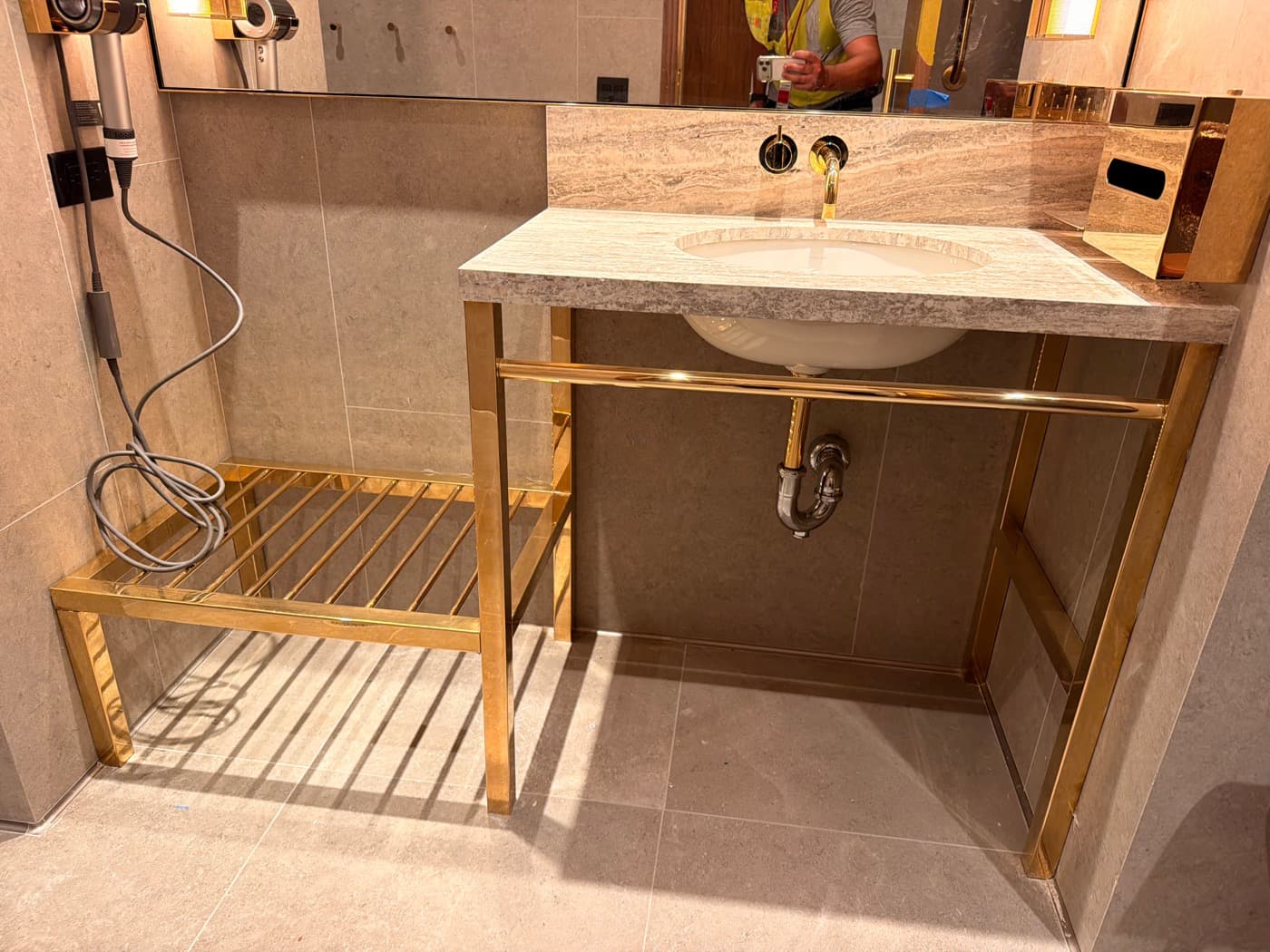 Bathroom featuring a veined stone vanity with brass-toned metal framing and slatted bench