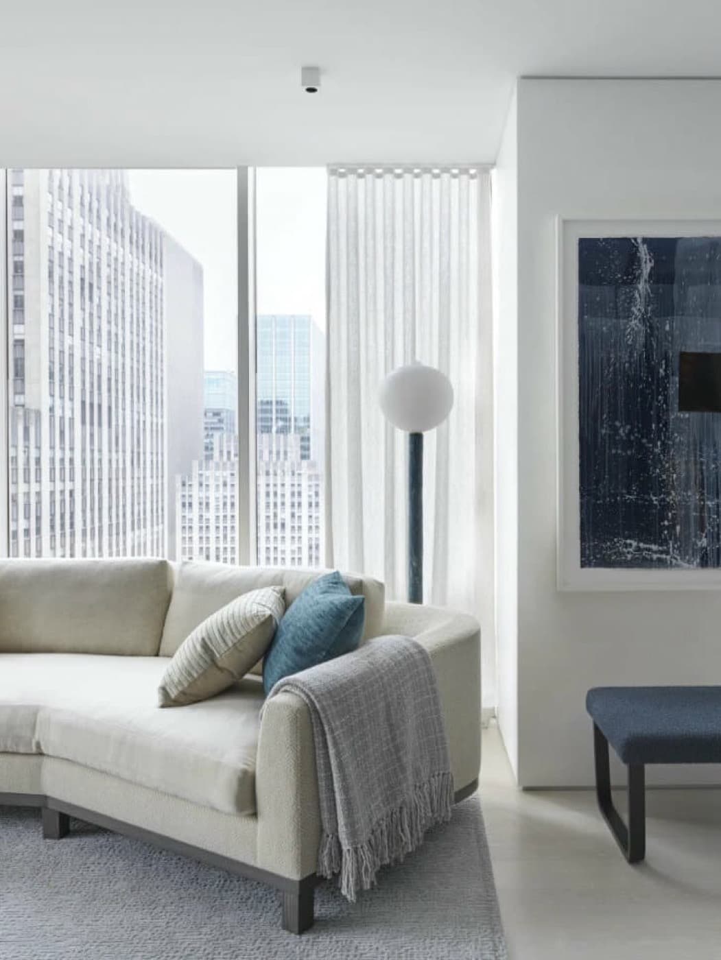 High-rise living room with floor-to-ceiling windows framing city views and curved neutral sofa