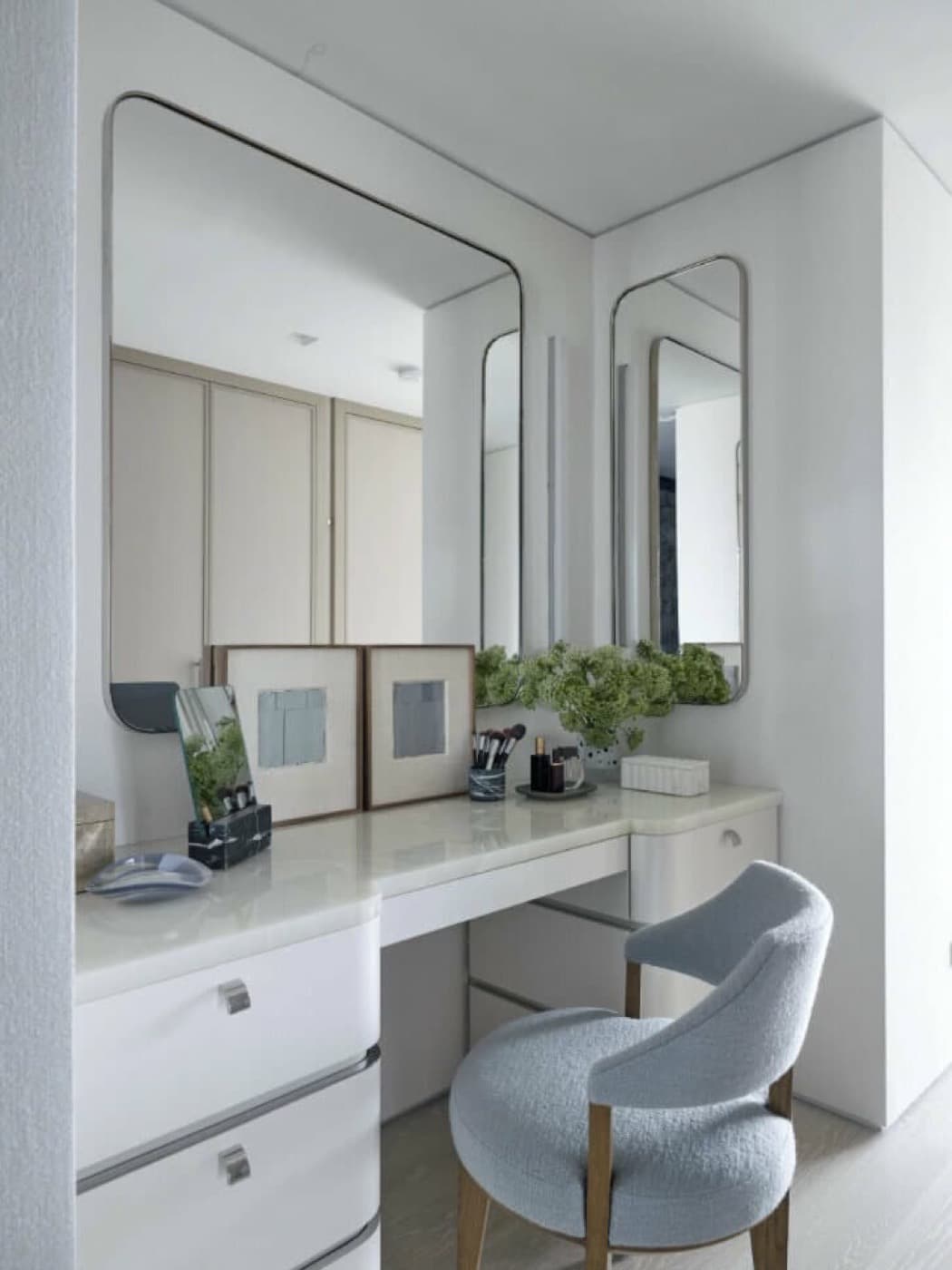Dressing nook with custom white vanity cabinetry, pale stone countertop, and rounded wall mirrors