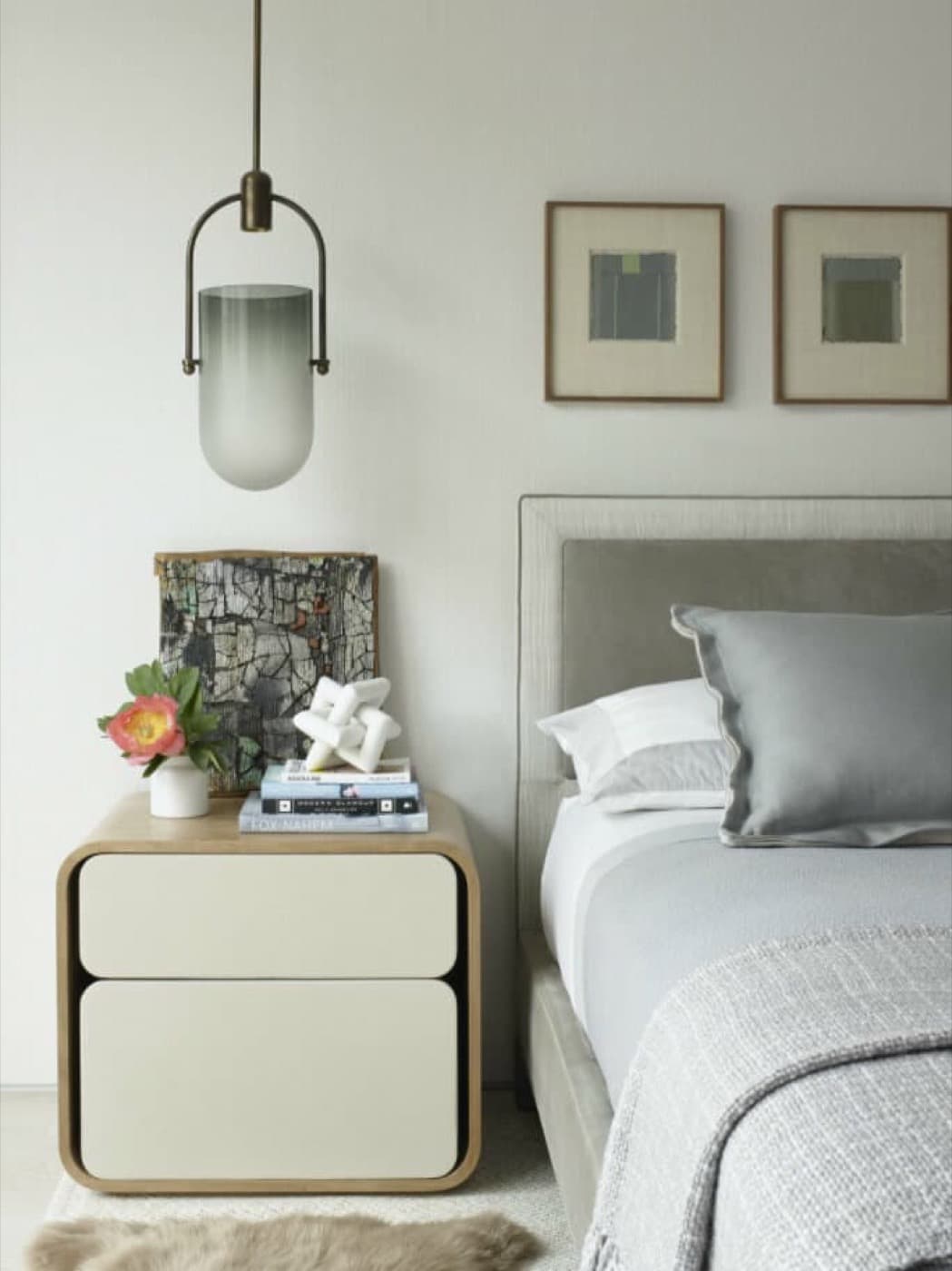 Bedroom with an upholstered headboard beside a curved timber nightstand and hanging pendant light