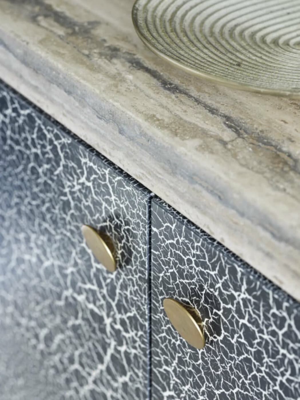 Interior millwork detail with crackled black cabinet fronts, brass hardware, and a veined stone countertop