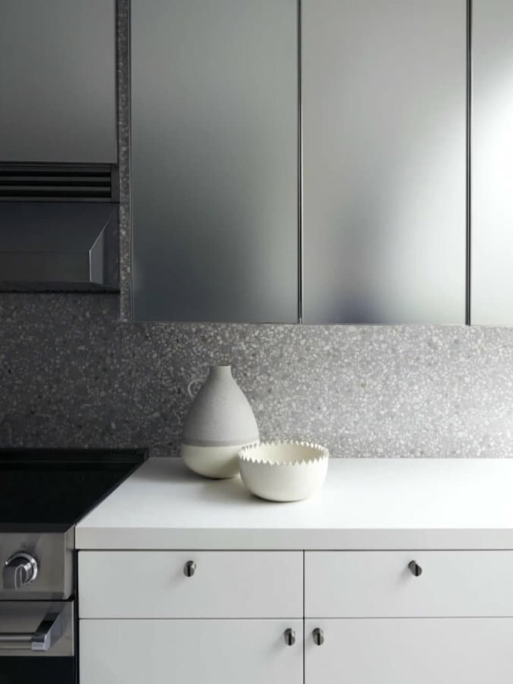 Kitchen detail with white base cabinetry, speckled grey backsplash, and sleek upper cabinets