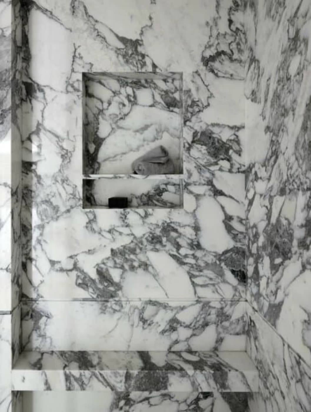 Bathroom shower lined in dramatically veined stone with a recessed niche and matching bench