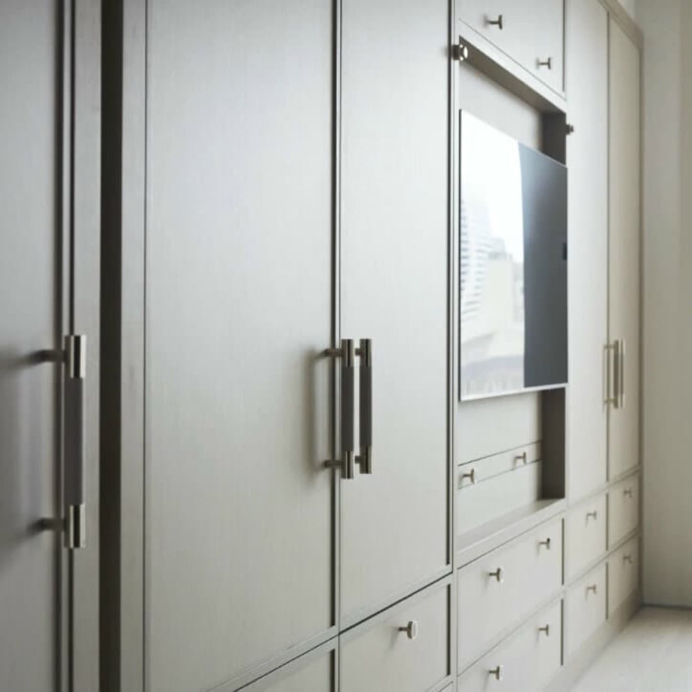 Built-in wardrobe millwork featuring full-height cabinet doors, lower drawers, and a recessed television niche