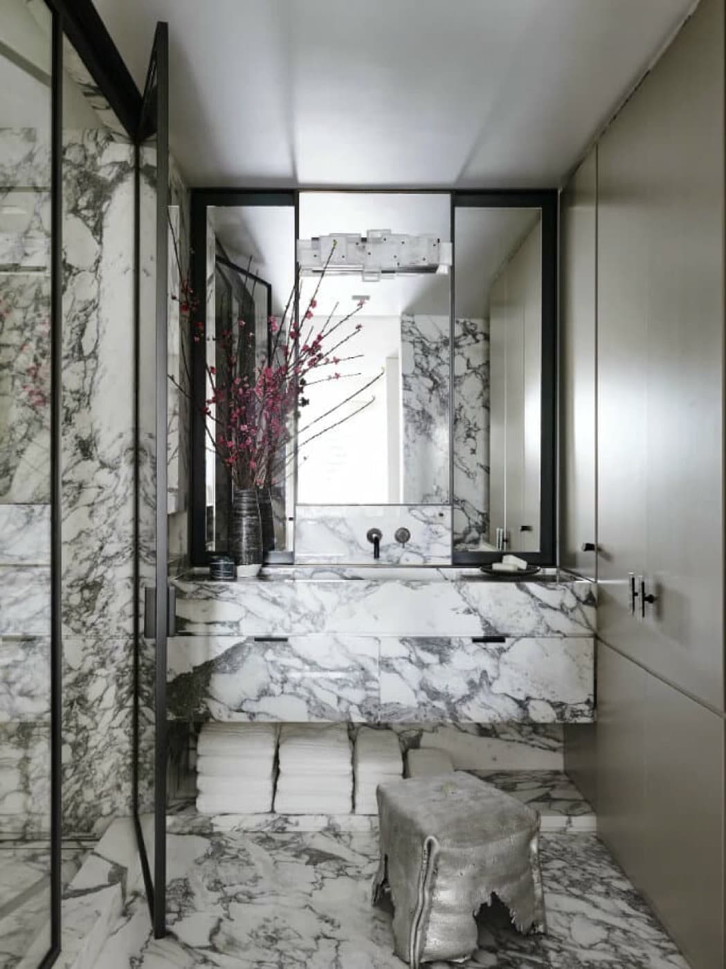 Bathroom with a floating veined stone vanity, stone wall cladding, and tall built-in cabinetry