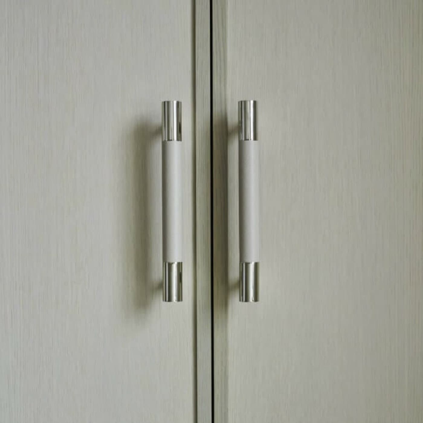 Built-in wardrobe detail showing pale timber doors with polished metal and wrapped pull handles