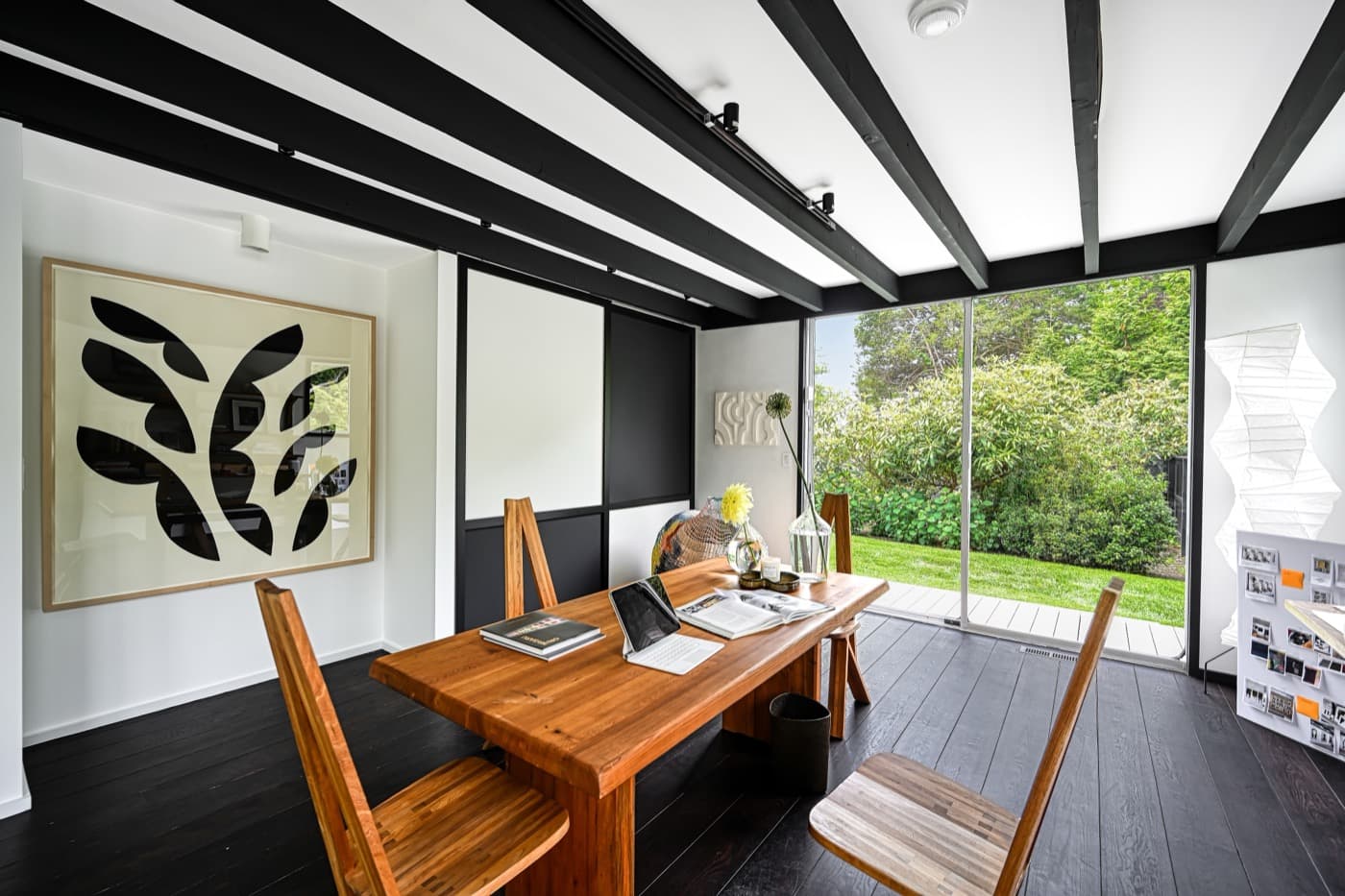 Modern dining area featuring exposed black ceiling beams, dark wood flooring, and sliding glass doors