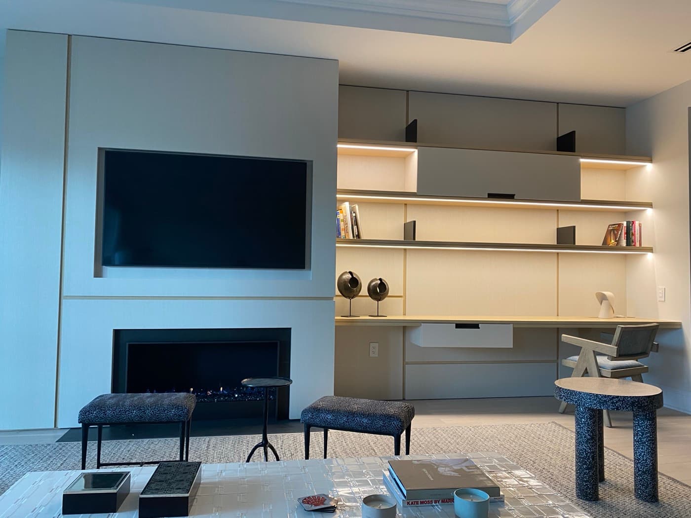 Living room featuring built-in fireplace wall, recessed television, and illuminated custom desk shelving