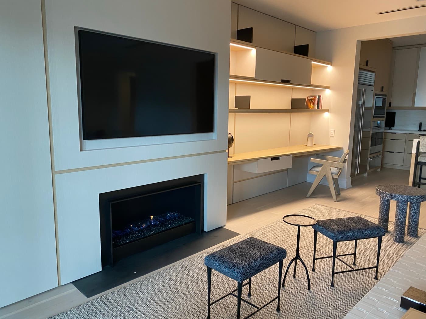 Modern living room featuring built-in fireplace panelling beside integrated illuminated desk cabinetry and shelving