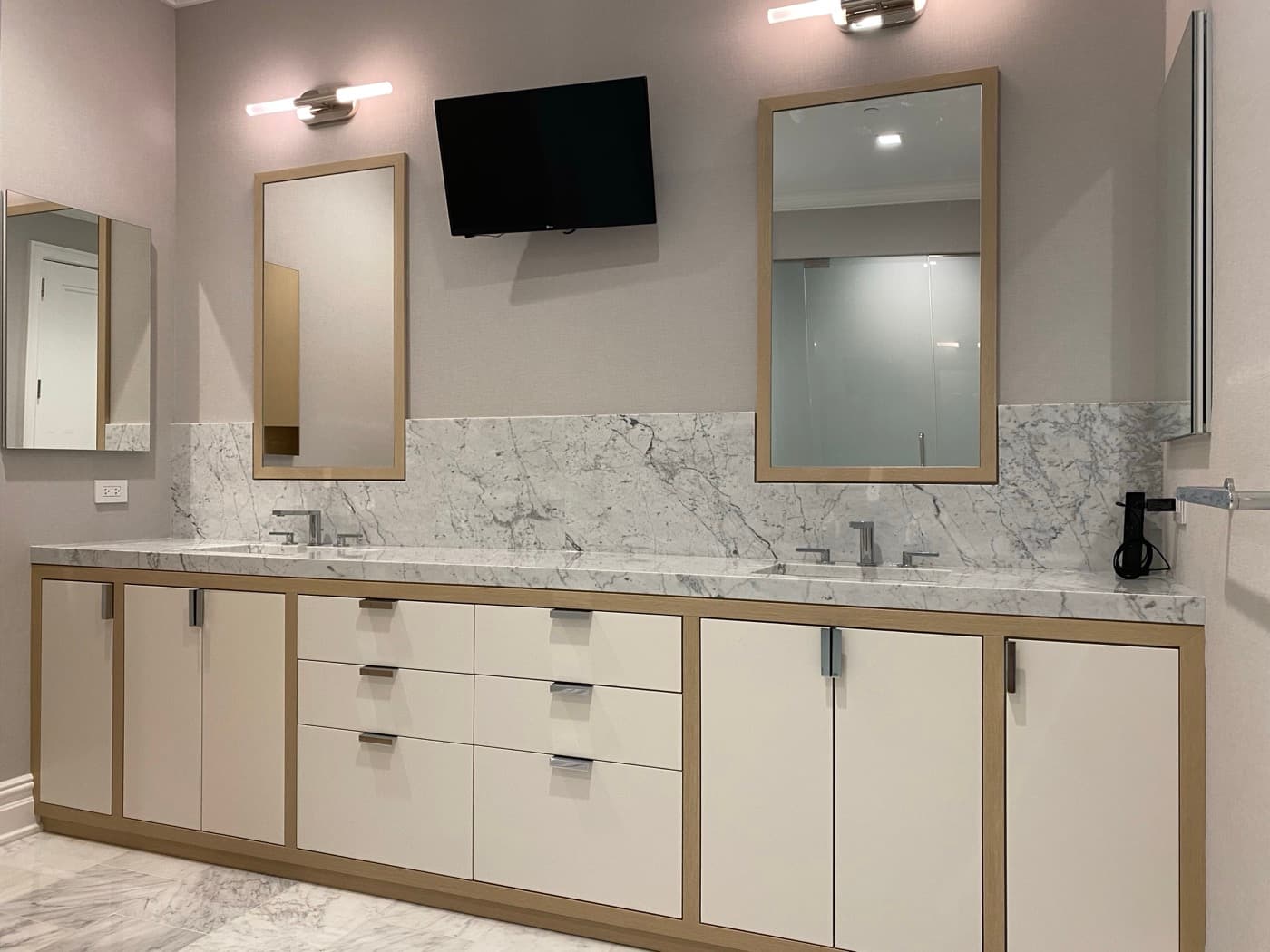 Bathroom double vanity with pale veined stone countertop, backsplash, and light timber-trimmed cabinetry