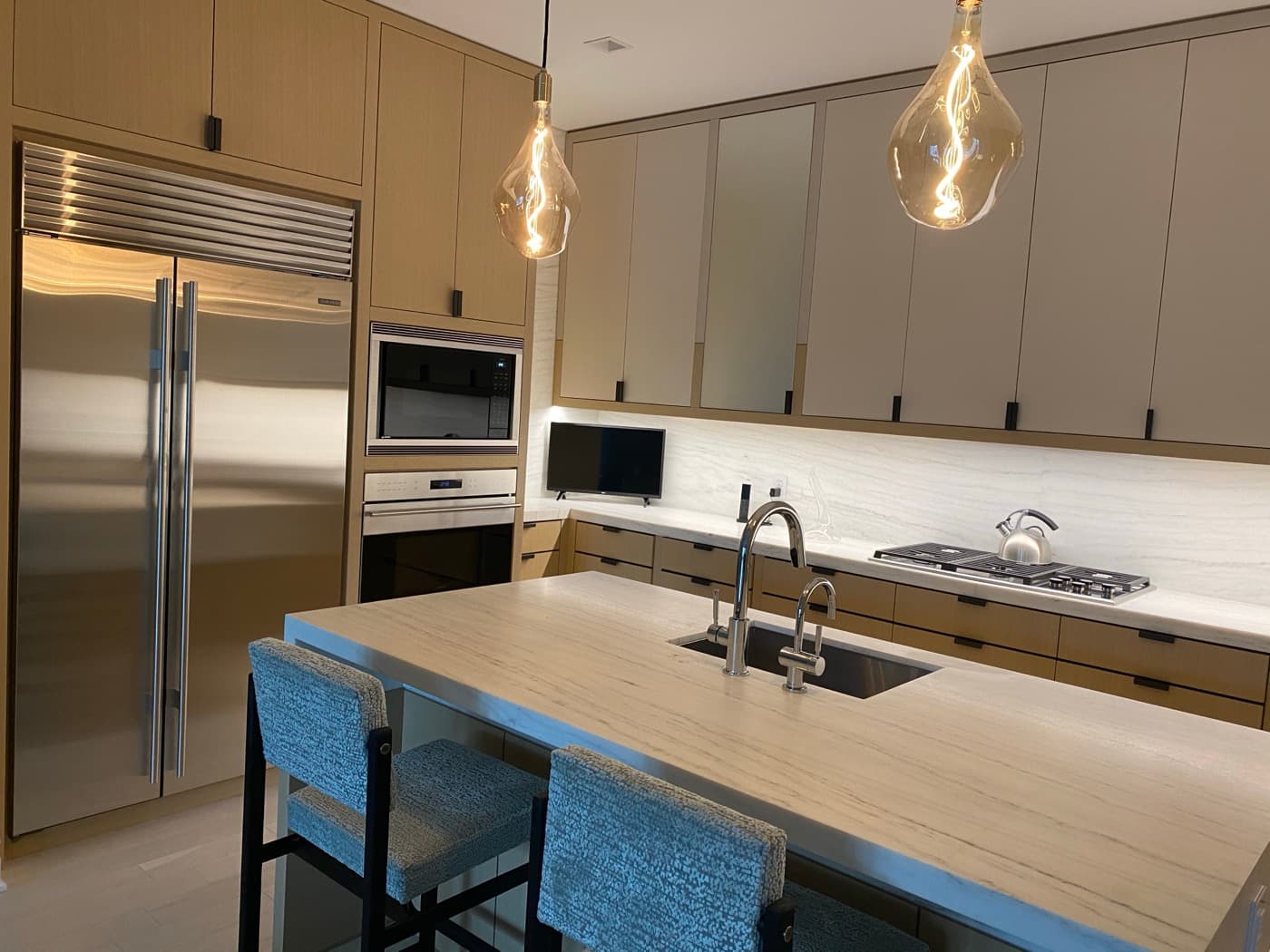 Contemporary kitchen featuring light timber cabinetry, pale stone island with sink, and integrated appliances