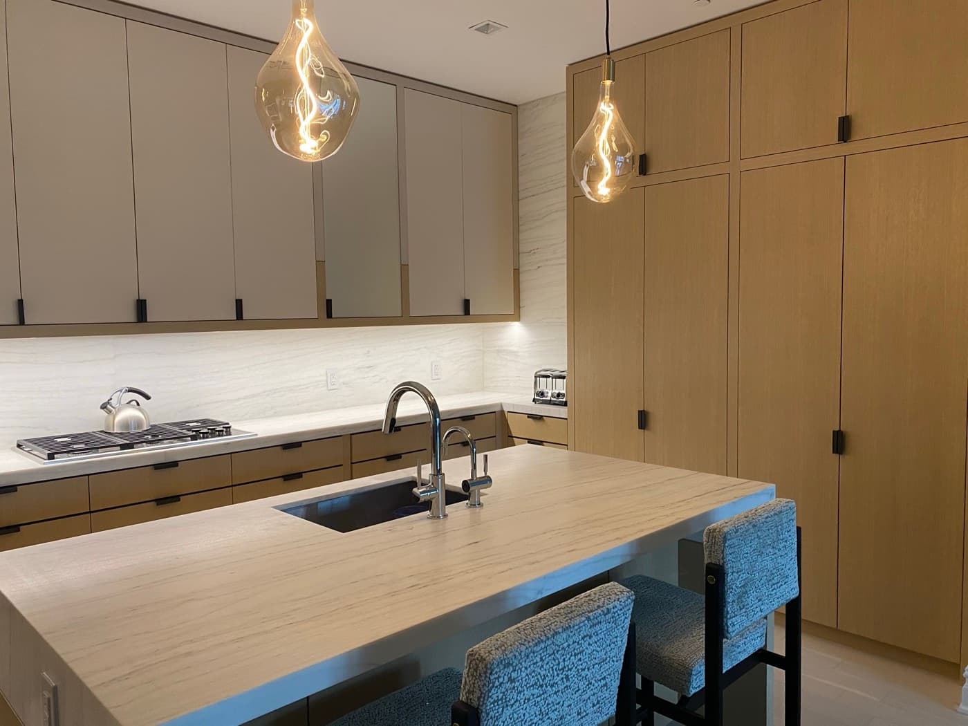 Kitchen with pale stone island countertop, undermount sink, and custom light timber cabinetry
