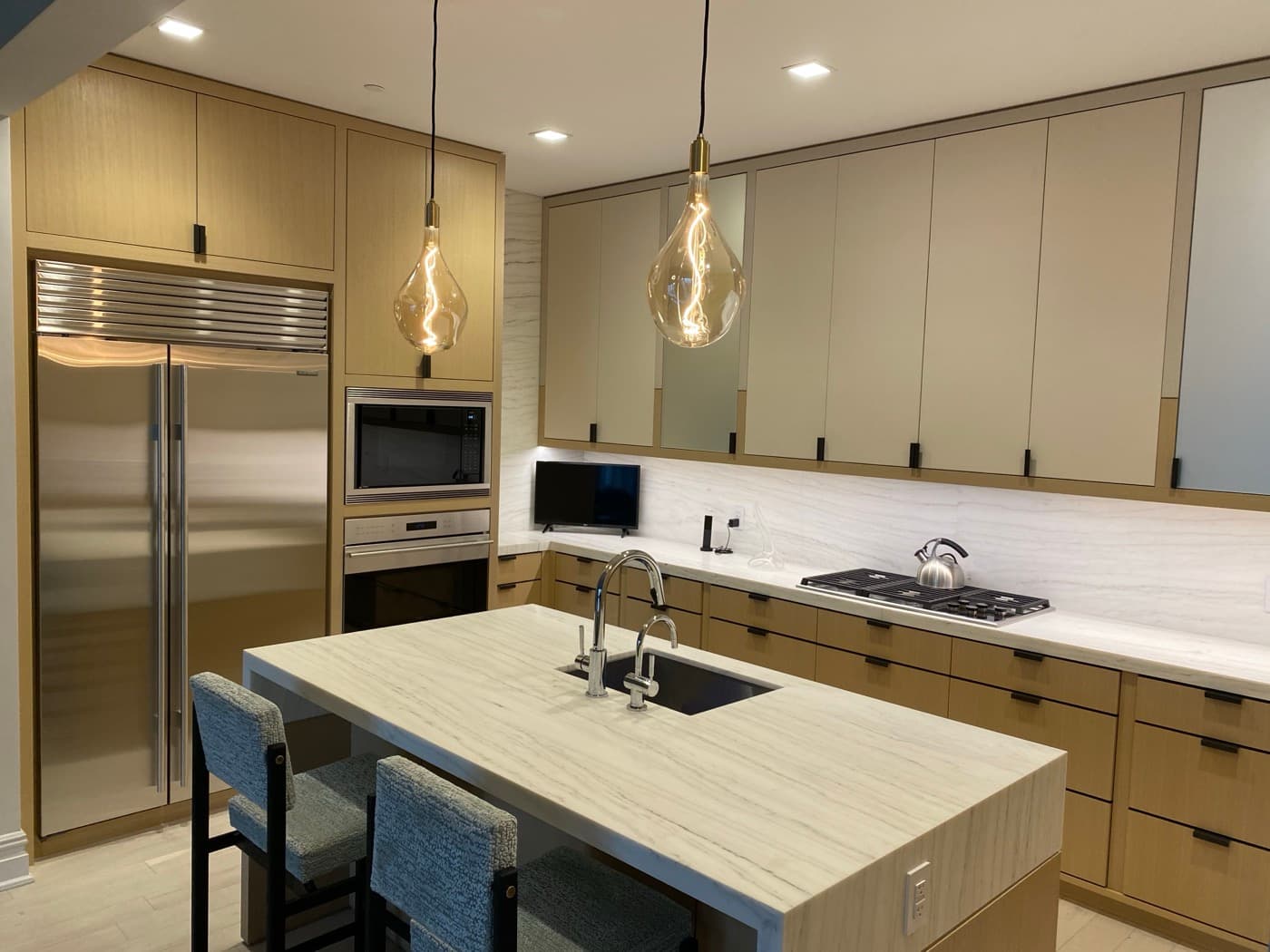 Kitchen with custom light timber cabinetry, pale stone island, and integrated stainless steel appliances