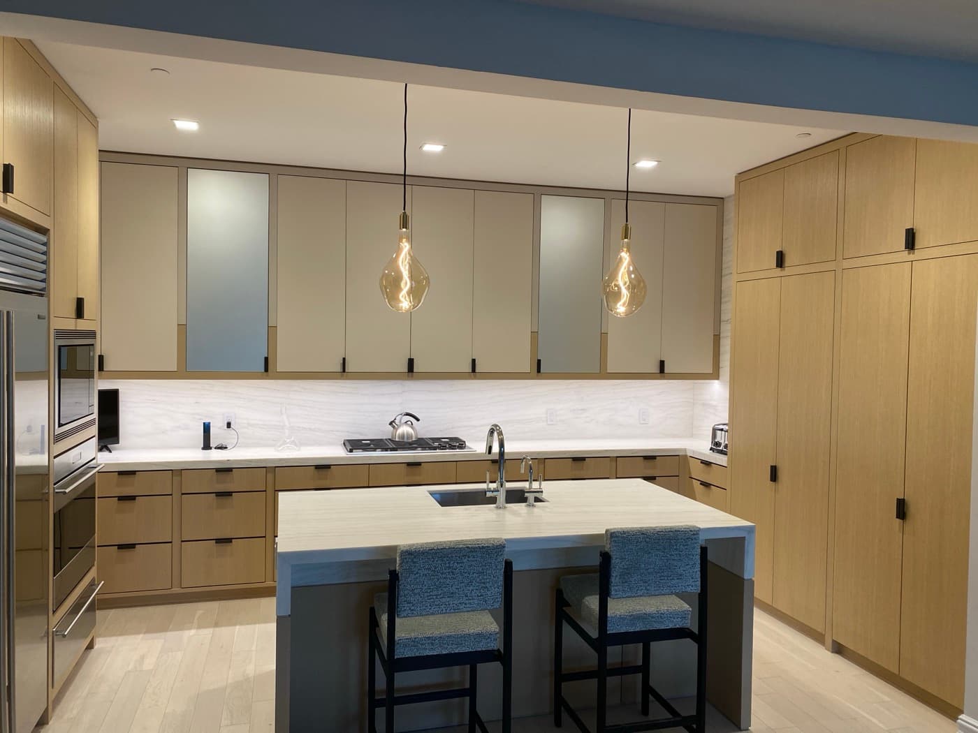 Modern kitchen with custom light timber cabinetry, pale stone island, and pendant lights
