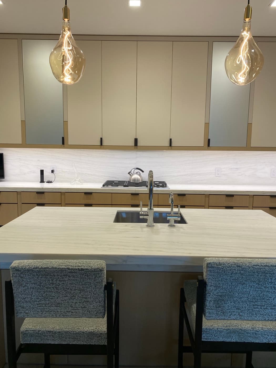 Modern kitchen featuring a pale veined stone island, minimalist cabinetry, and glass pendant lighting