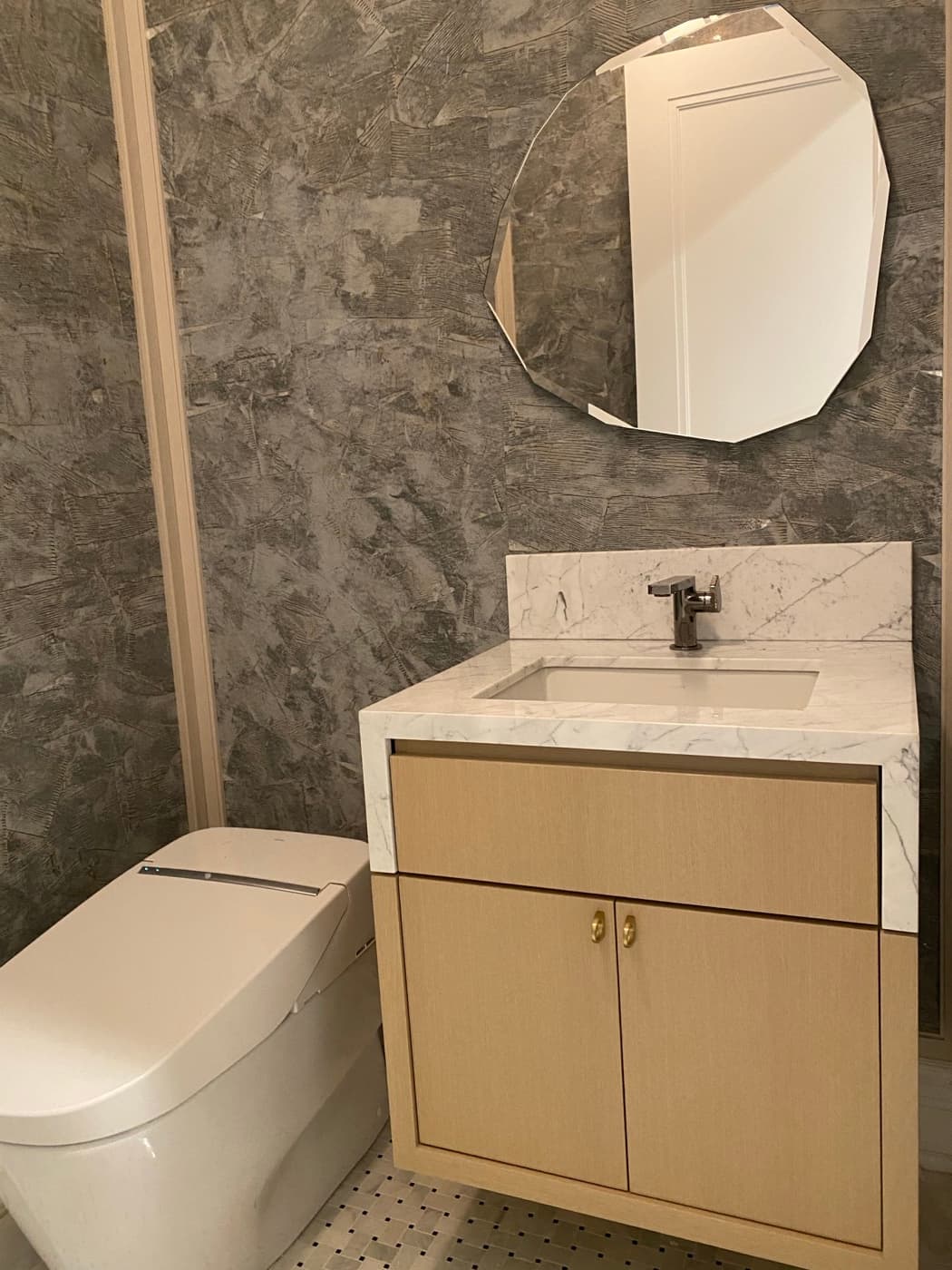 Powder room featuring light timber vanity with pale veined stone countertop and geometric mirror