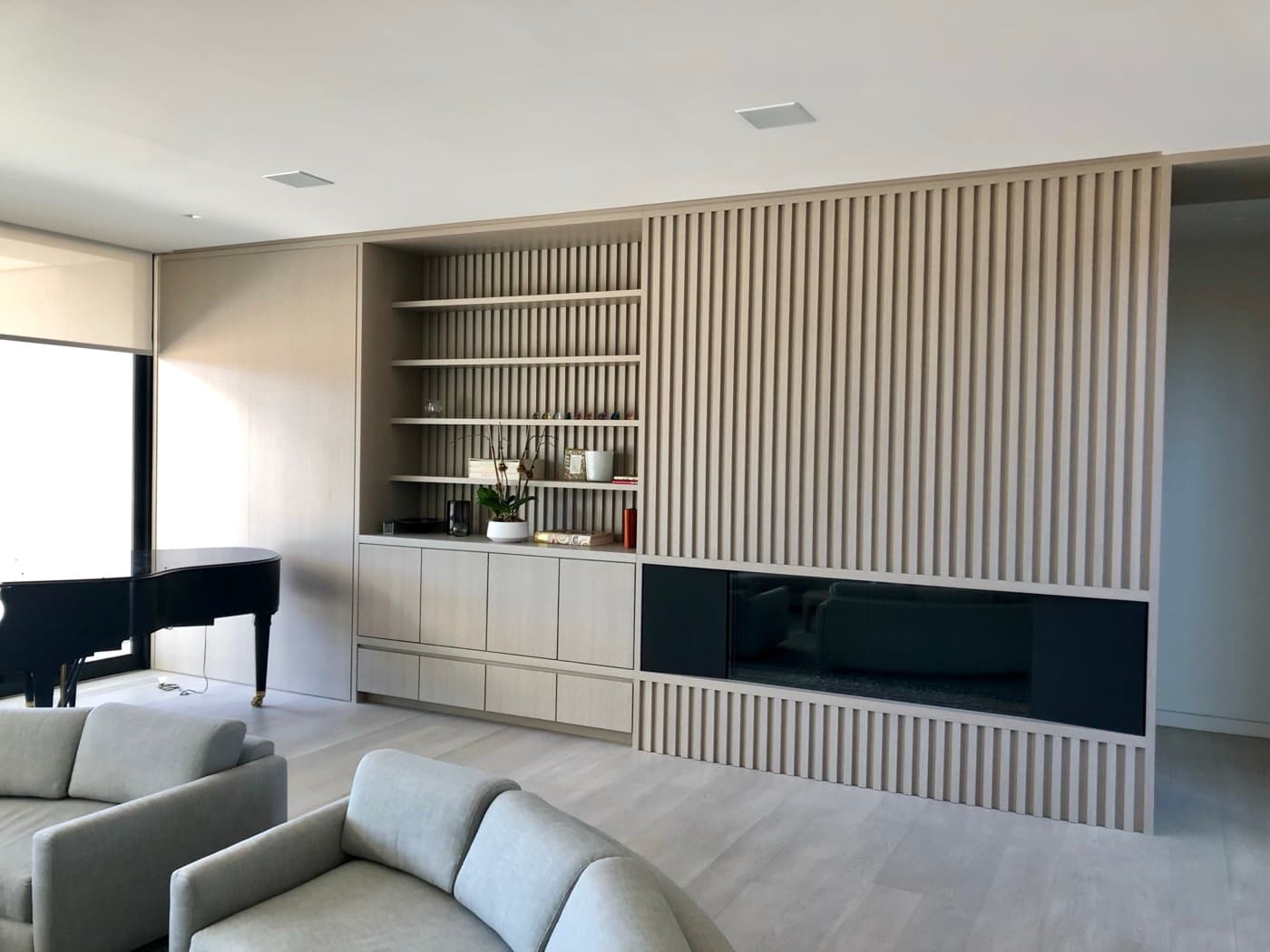 Living room with pale timber millwork, open shelving and a slatted feature wall
