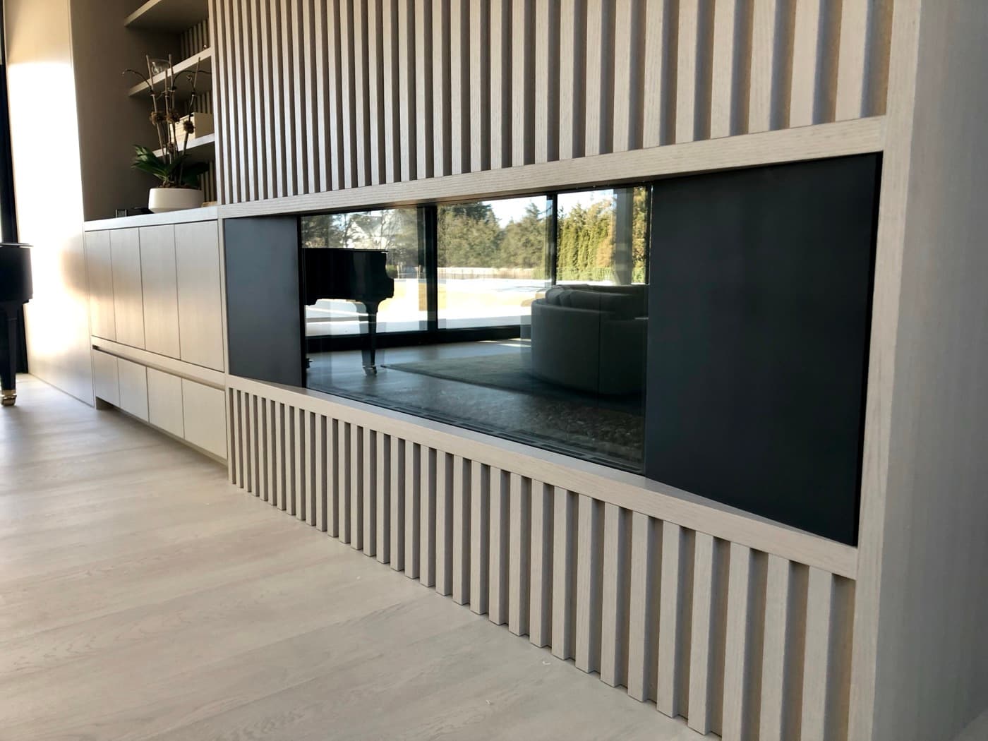 Living room featuring pale timber slatted panelling around a see-through glass fireplace and cabinetry