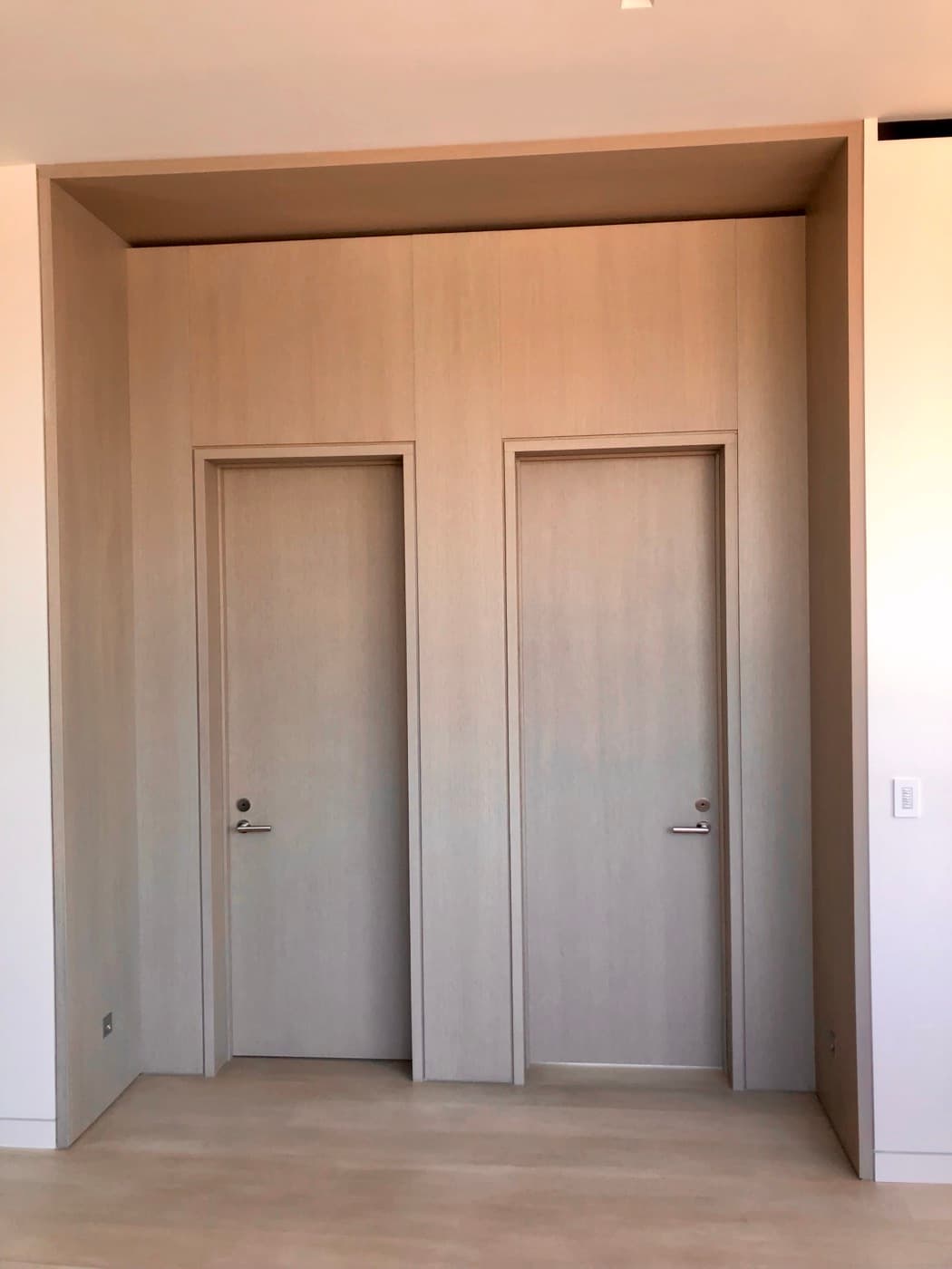 Hallway alcove featuring custom pale timber wall panelling with two integrated matching flush doors