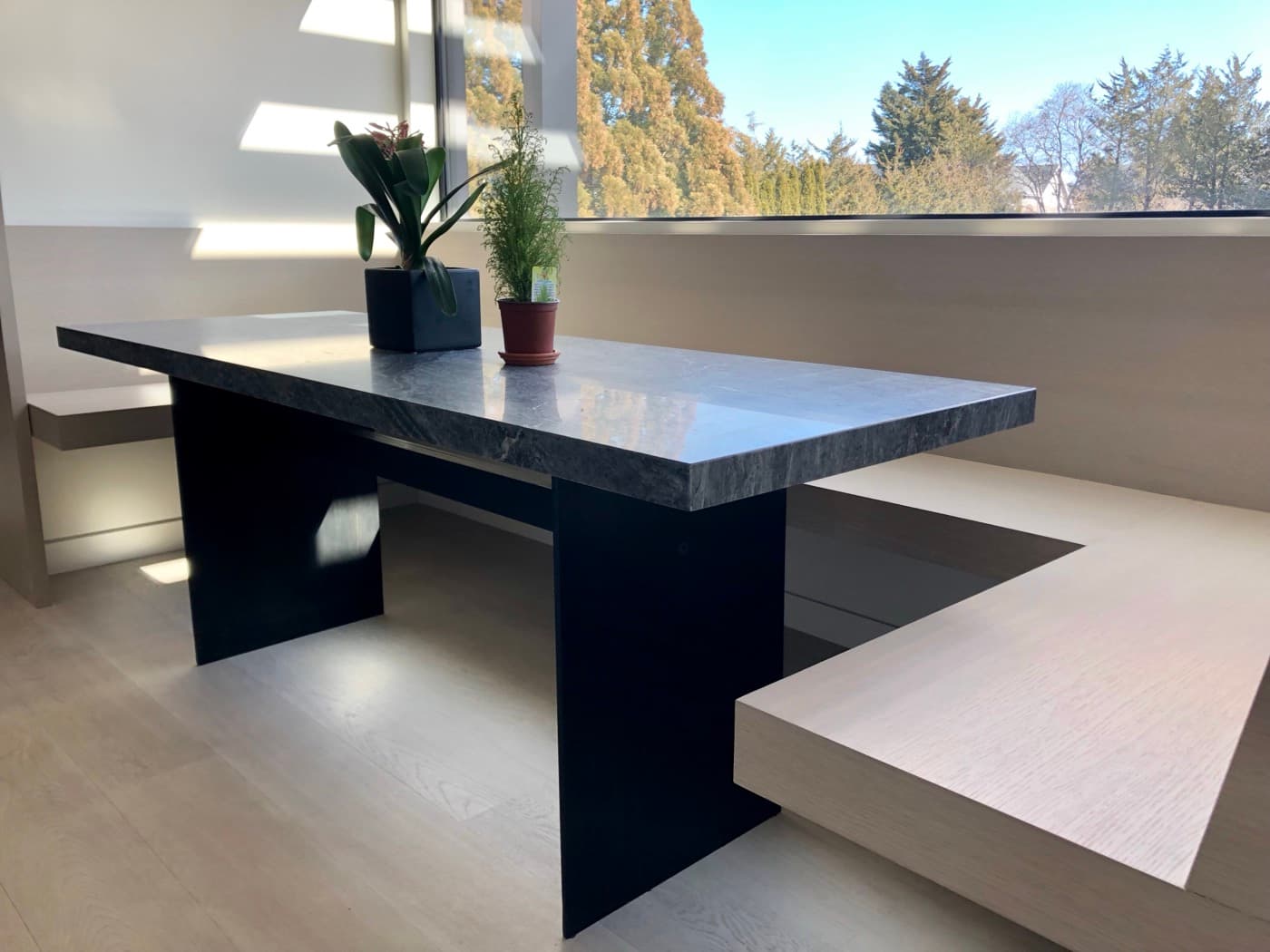 Dining nook with built-in pale timber banquette seating and a grey stone dining table