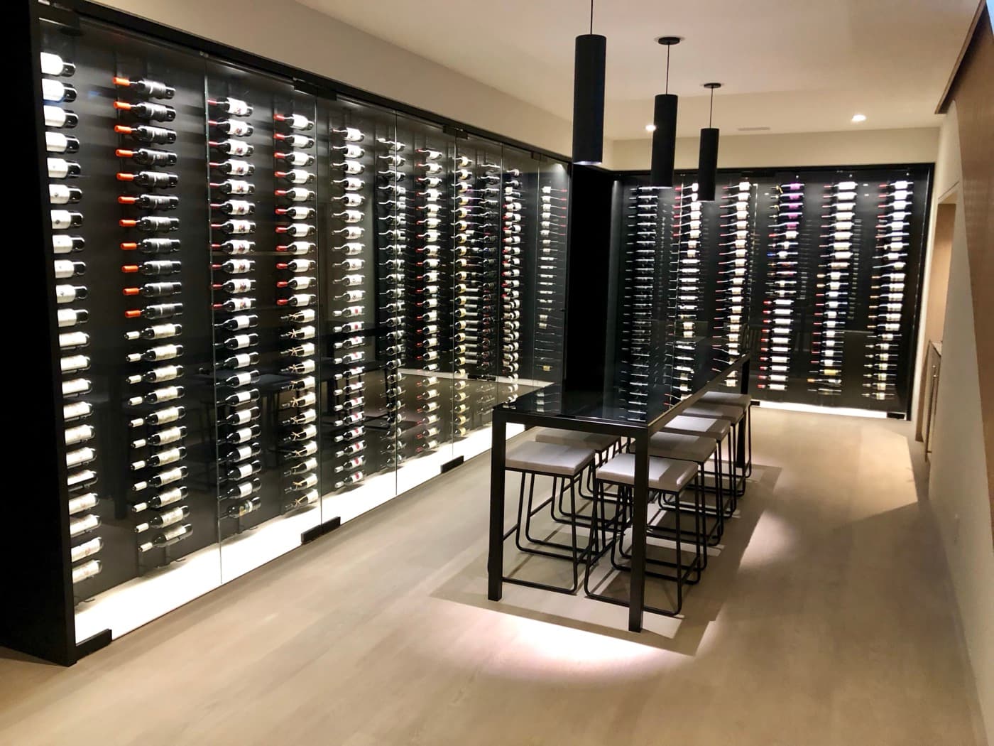 Wine cellar with glass-enclosed illuminated wine racks and a central dark metal tasting table