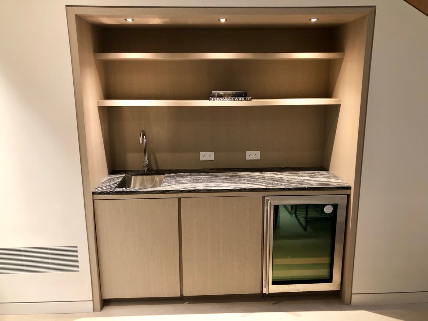 Built-in wet bar niche with pale timber millwork, open shelves, and dark veined stone countertop