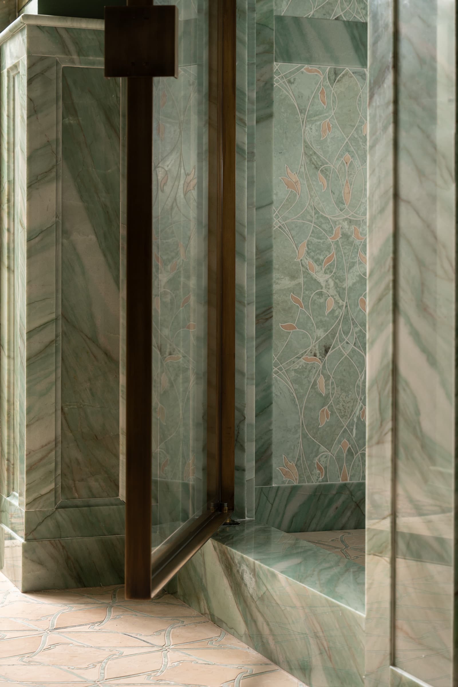 Bathroom shower entrance with green veined stone panelling, decorative inlay, and dark metal glass door
