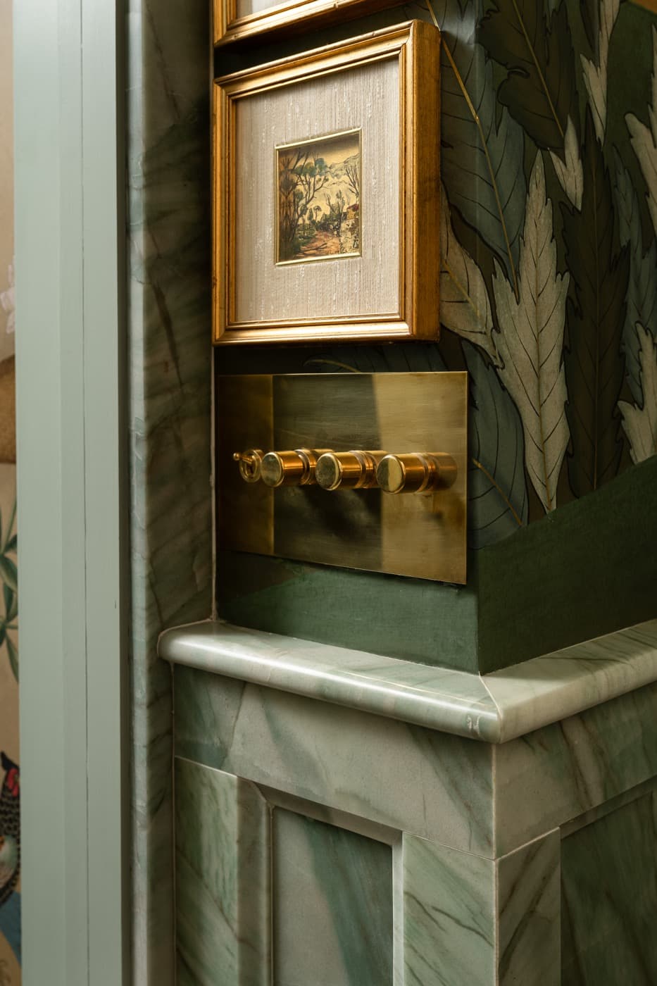 Interior corner with green veined stone wainscoting, brass switchplate, and botanical wallpaper