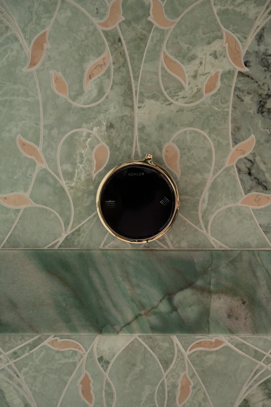 Shower wall with green floral inlaid stone tile and round digital shower control fixture