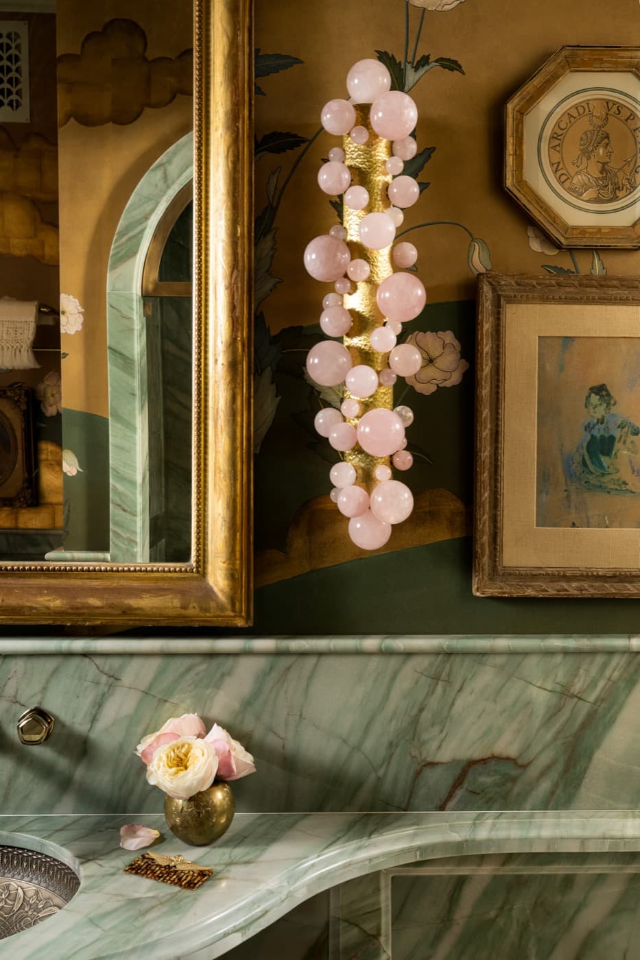 Powder room with green veined stone vanity counter, gilt-framed mirror, and sculptural wall sconce