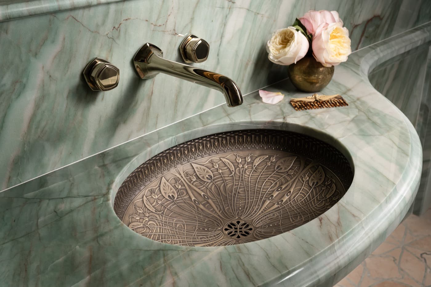 Bathroom vanity with green veined stone countertop, ornate patterned metal sink, and wall-mounted faucet