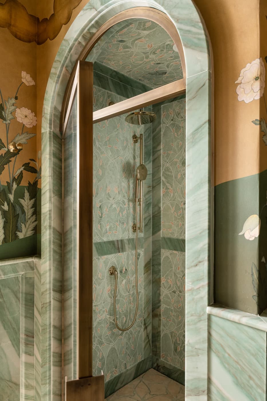 Bathroom shower with arched green veined stone surround, brass-toned fixtures, and patterned stone interior