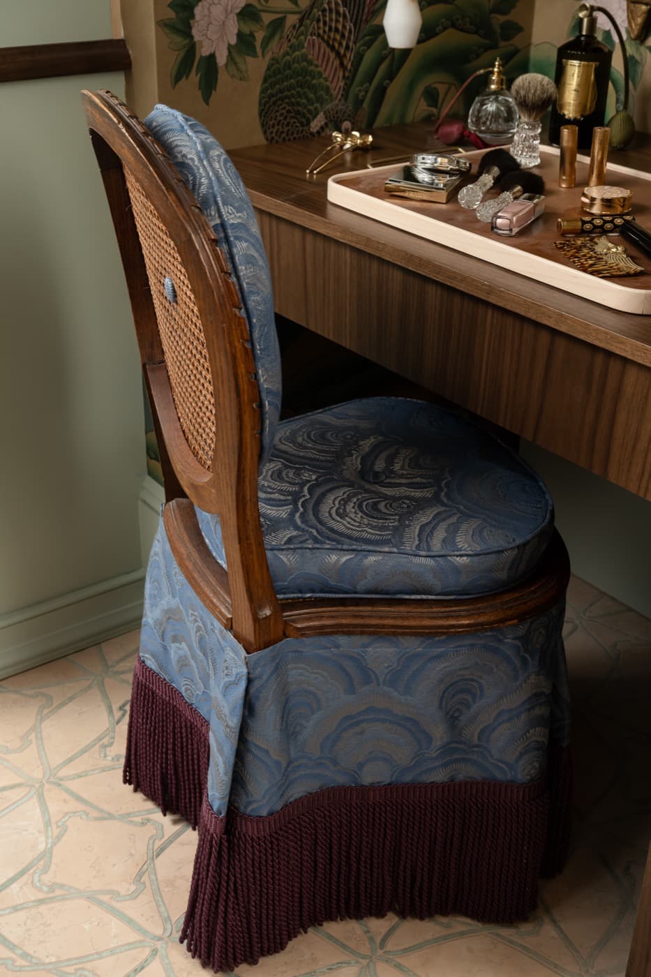 Dressing room detail with a timber vanity desk and fringed upholstered cane-back chair