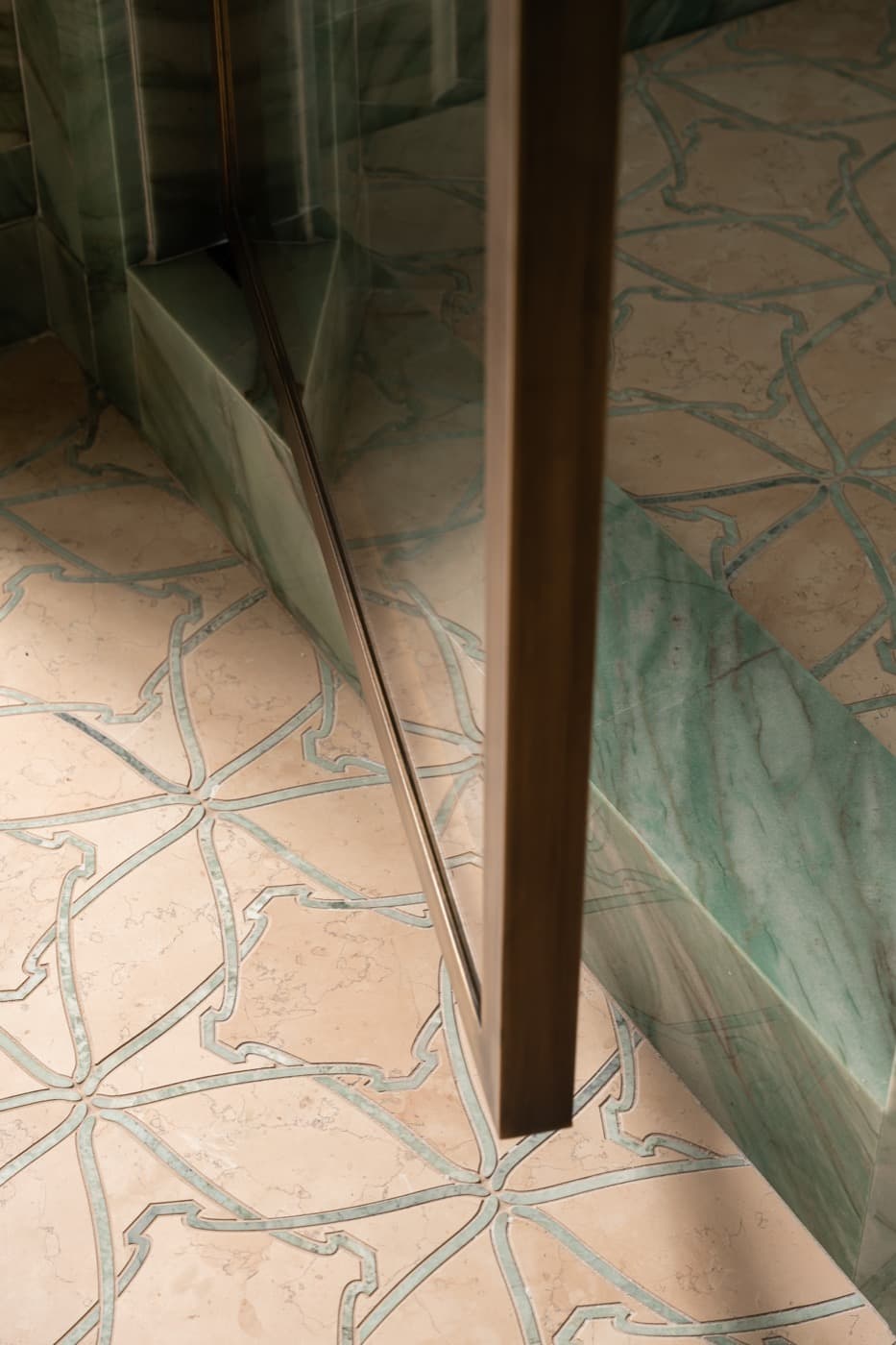 Bathroom detail showing metal-framed glass shower door, green veined stone curb, and patterned floor