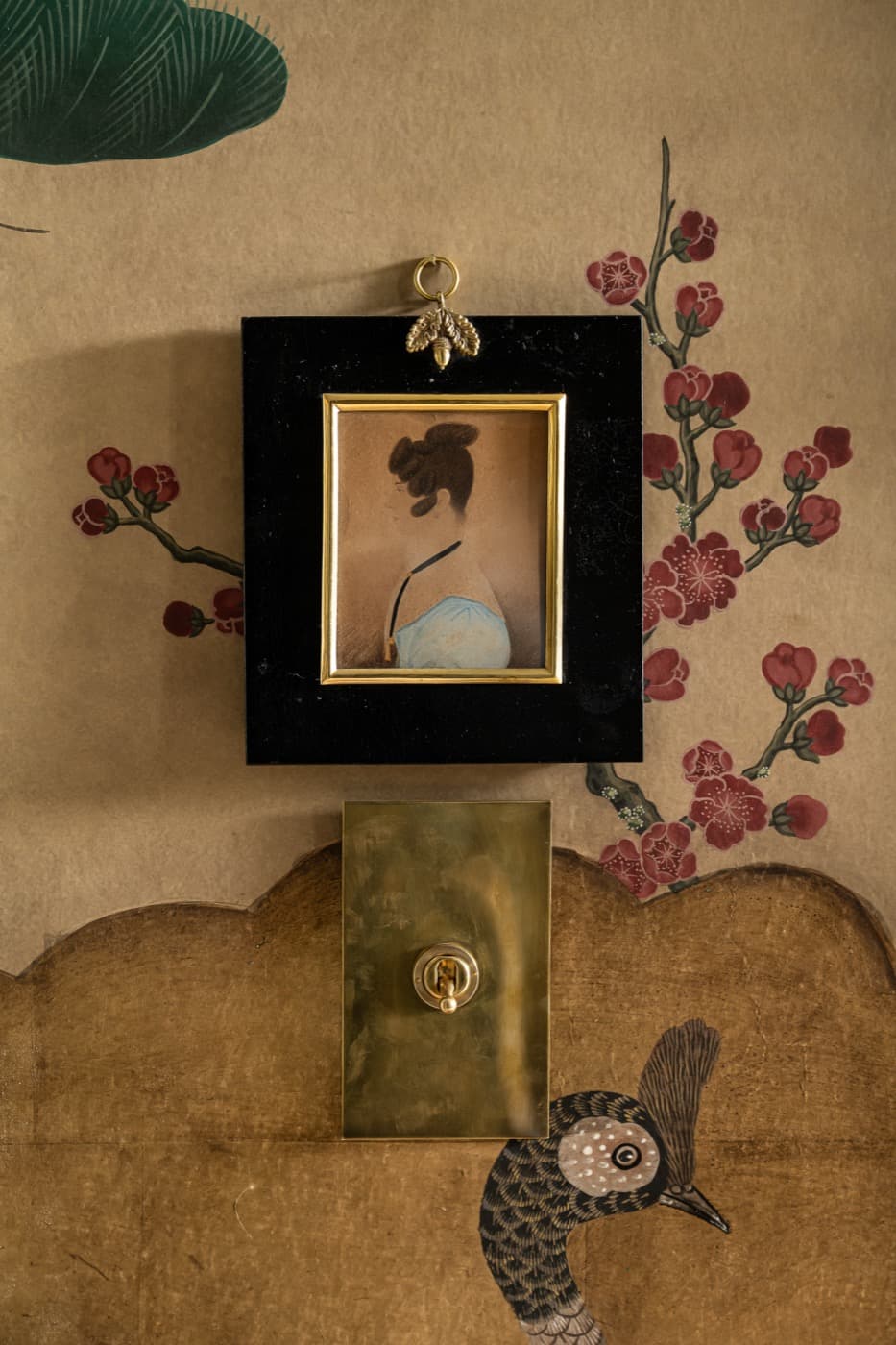 Interior wall featuring a brass-toned toggle switch beneath framed portrait on decorative wallpaper