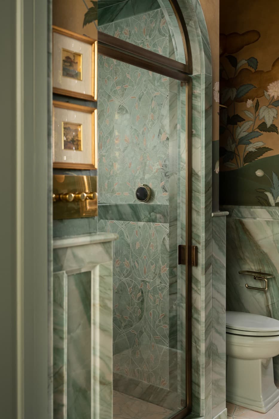 Bathroom with an arched shower enclosure trimmed in green veined stone and patterned tile
