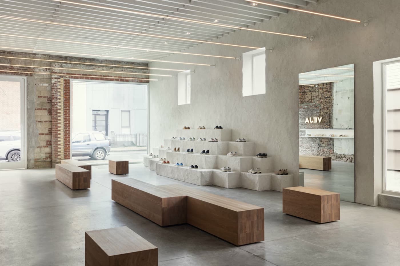 Retail showroom with tiered pale stone display pedestals, timber block benches, and linear overhead lighting