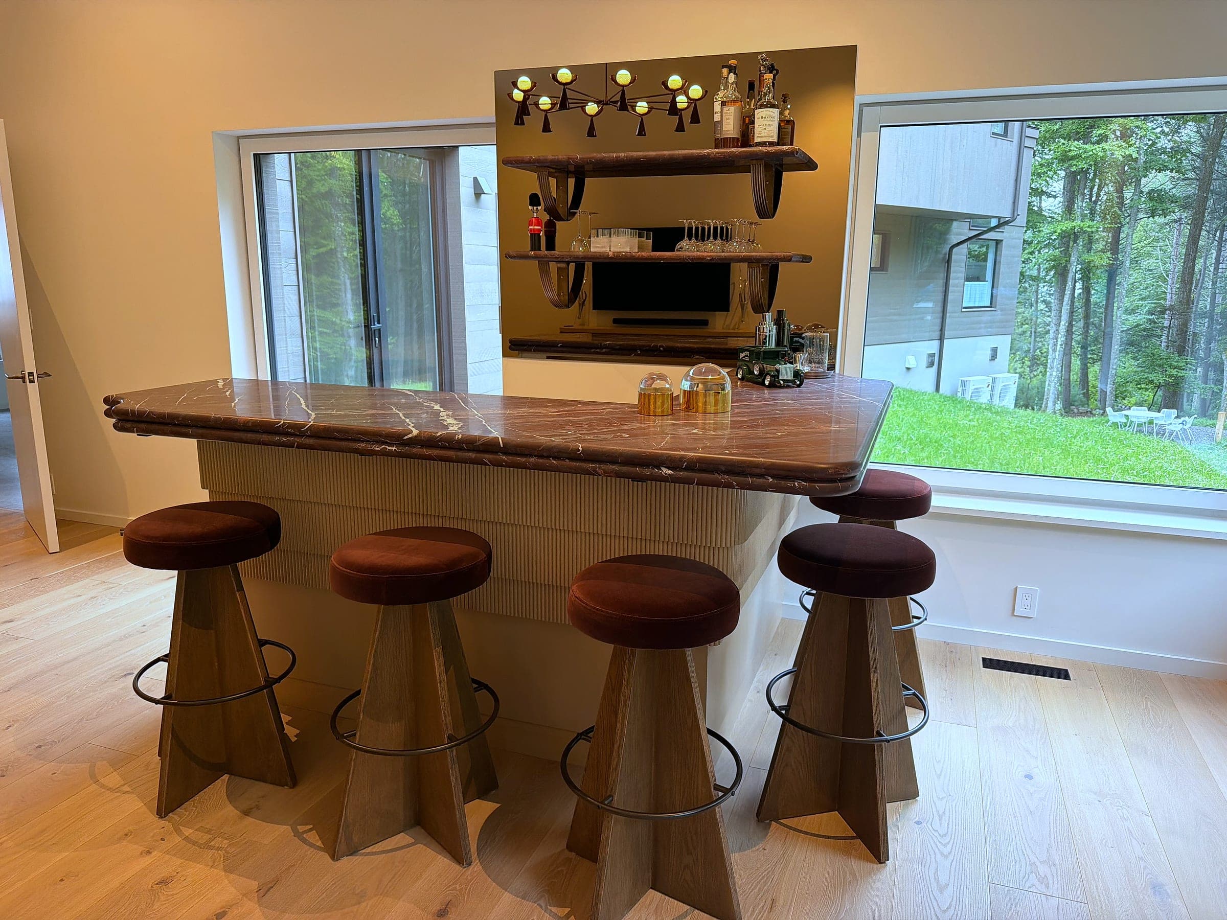 Bar with a fluted rift-sawn white oak base and a Rosso Levanto marble top, four upholstered stools, and open shelving on a bronze mirrored panel behind